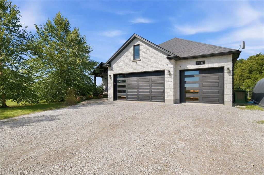 Stone exterior with a shingled roof, two attached garages with modern doors, and a gravel driveway