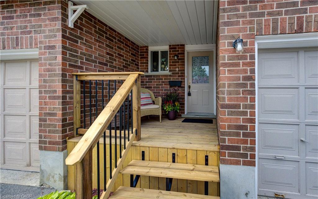 Brick exterior featuring a wood-finish porch with railing, a paneled entry door, and an exterior wall lantern