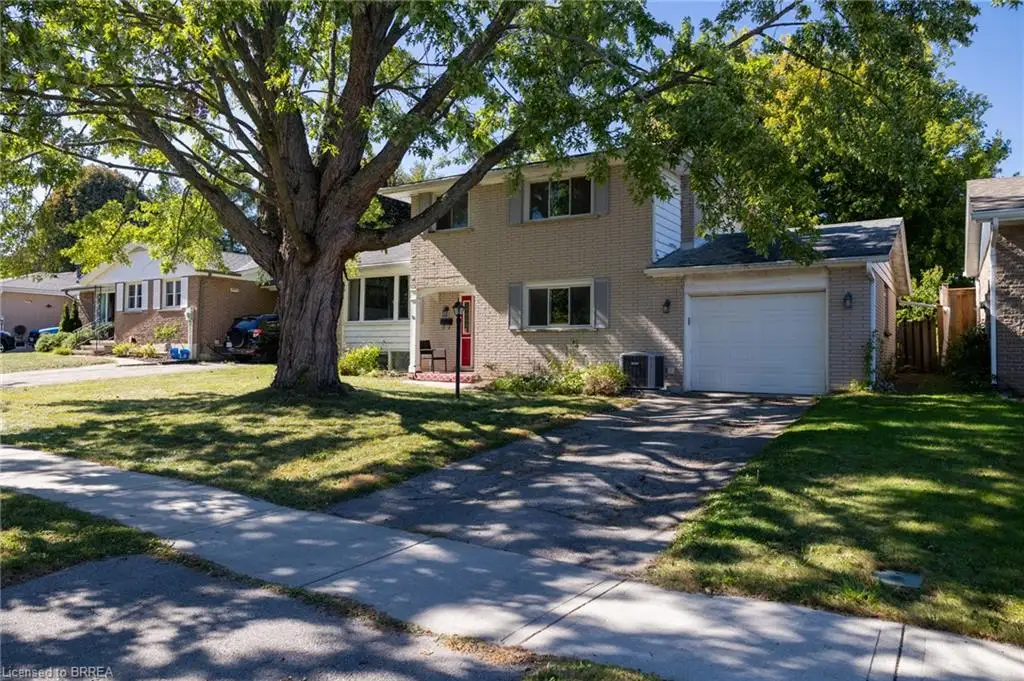 Two-story residence with a light-colored brick exterior, attached single-car garage, red entry door, and a mature shade tree in the front yard