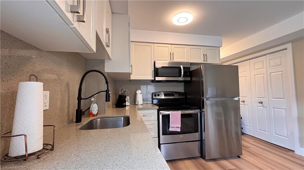 Modern kitchen featuring stainless steel appliances, light-toned cabinetry, a pull-down faucet, and a light-colored countertop