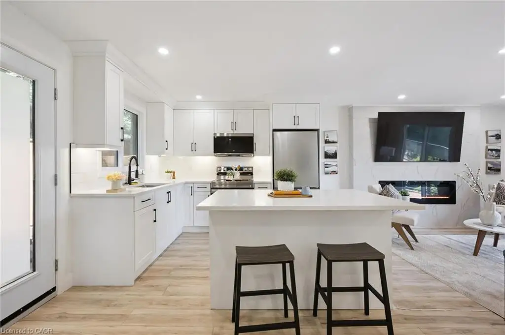 Kitchen featuring white shaker-style cabinetry, quartz countertops, a central island, wood-finish flooring, and a fireplace with a stone-surround wall