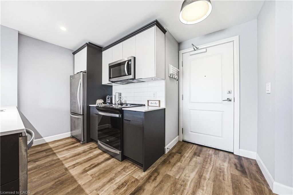 Compact kitchen featuring wood-finish flooring, two-tone cabinetry with white upper and dark lower units, stainless steel appliances, white subway tile backsplash, and light countertops