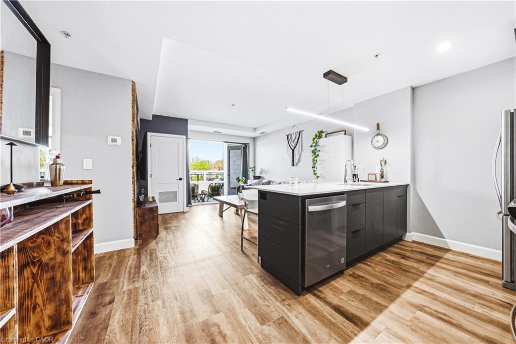 Kitchen island with a white countertop and dark cabinetry, stainless steel dishwasher, wood-finish flooring, and a sliding glass door to an outdoor space