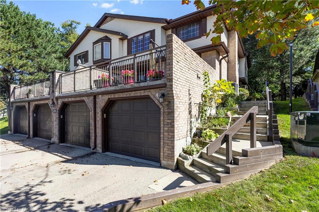 Multi-level residence featuring brick and siding exterior, multiple garage bays, a second-story balcony with metal railings, and exterior wooden stairs leading to the upper entry