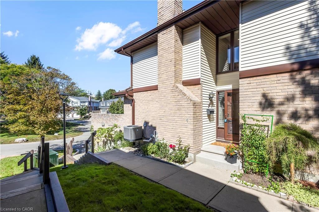 Brick and siding exterior with a prominent chimney, concrete walkway, and landscaped garden beds