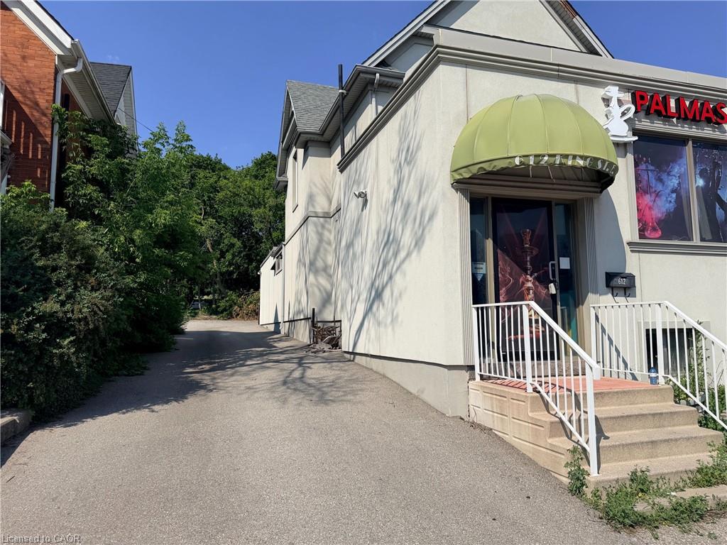 Building exterior featuring a light-colored stucco finish, a green fabric awning, and a prominent entrance with concrete steps and white railings