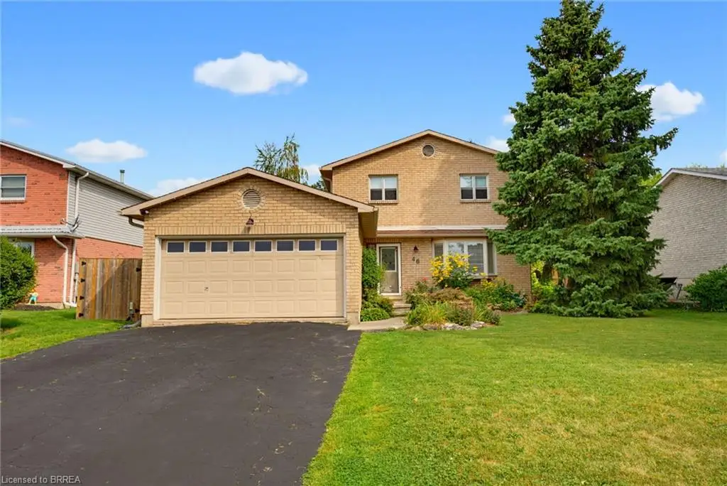 Brick and stucco exterior with an attached garage, paved driveway, and mature landscaping