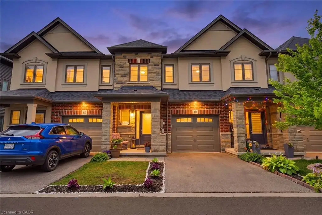 Modern townhome exterior featuring stone and brick accents, a gabled roofline, an attached garage, a covered front entry, and a paved driveway