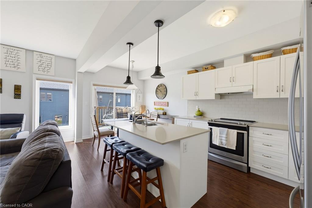 Open-concept kitchen featuring an island with pendant lighting, white cabinetry, integrated stainless steel appliances, light-toned countertops, and wood-finish flooring