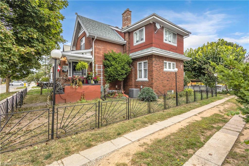 Brick exterior with white-framed windows, a covered front entry, and a decorative black metal fence