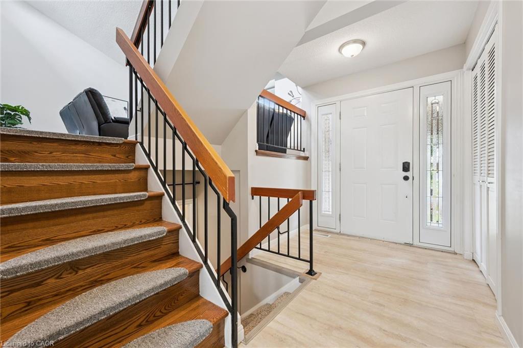 Wood-finish flooring, white paneled entry door with decorative glass sidelights, and a wood and metal staircase with carpeted treads