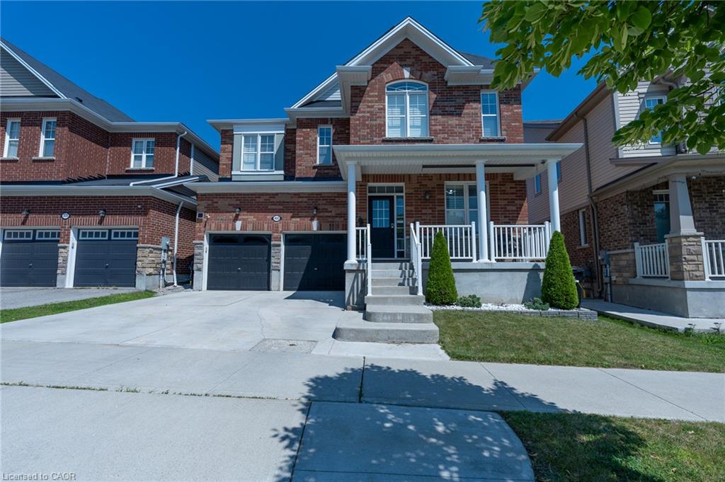 Brick facade with stone accents, covered front porch, concrete driveway, attached garage, and manicured front lawn