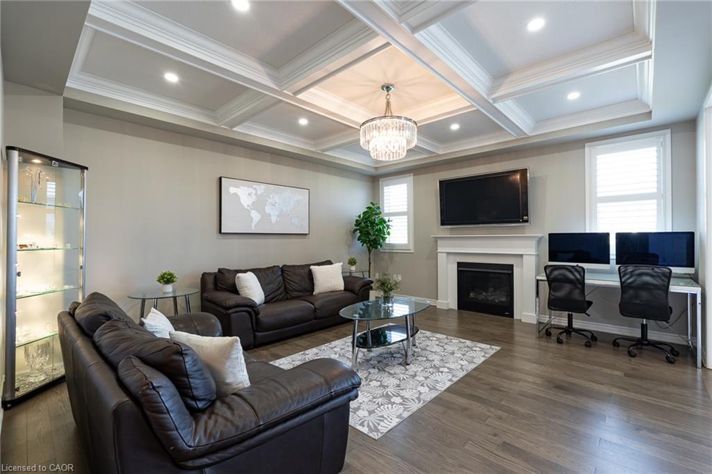 Coffered ceiling with recessed lighting and a chandelier, wood-finish flooring, white fireplace with mantle, and window shutters
