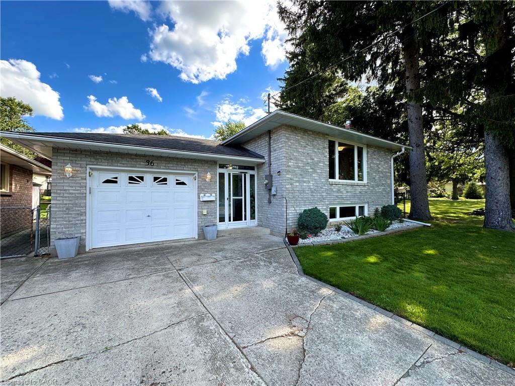 Brick exterior with an attached garage, landscaped front garden, and mature trees