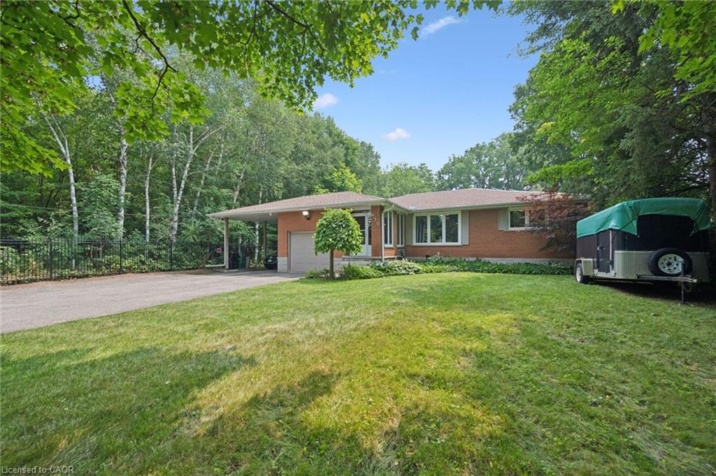 Brick-clad residence featuring a front lawn, paved driveway, and mature perimeter trees, featuring a spacious front lawn with irrigation.