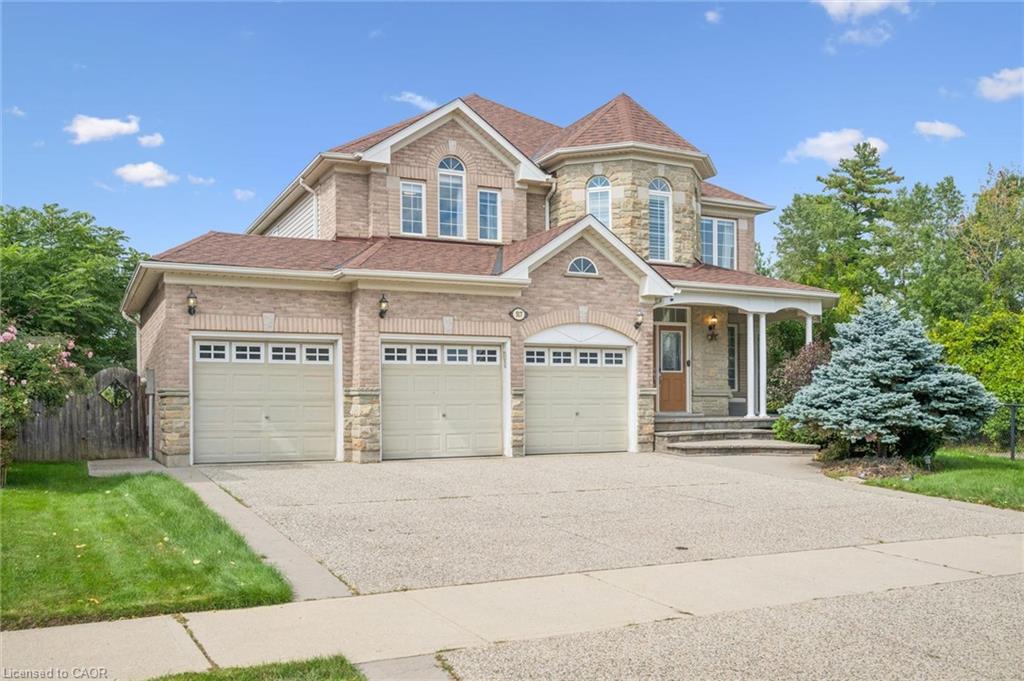 Brick and stone exterior with a turret feature, three-car garage, covered entry porch, and mature landscaping