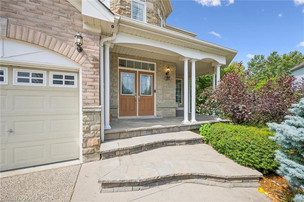 Stone exterior with brick accents, covered front porch, double entry doors with decorative glass, and a paved stone walkway