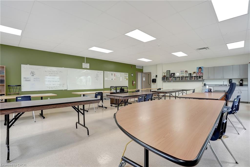 This versatile space features a vibrant green accent wall, whiteboards for presentations, and a functional kitchenette with cabinetry and a sink