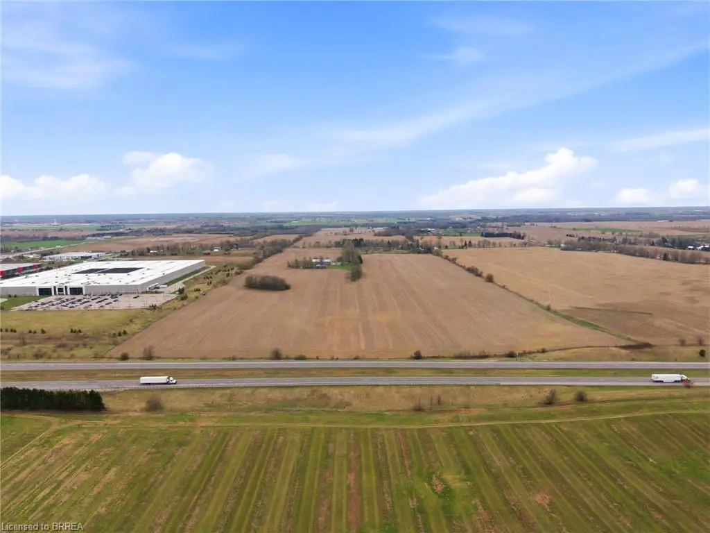 Expansive agricultural land featuring a paved multi-lane highway, bordering a large commercial facility with extensive parking, and surrounded by additional cultivated fields