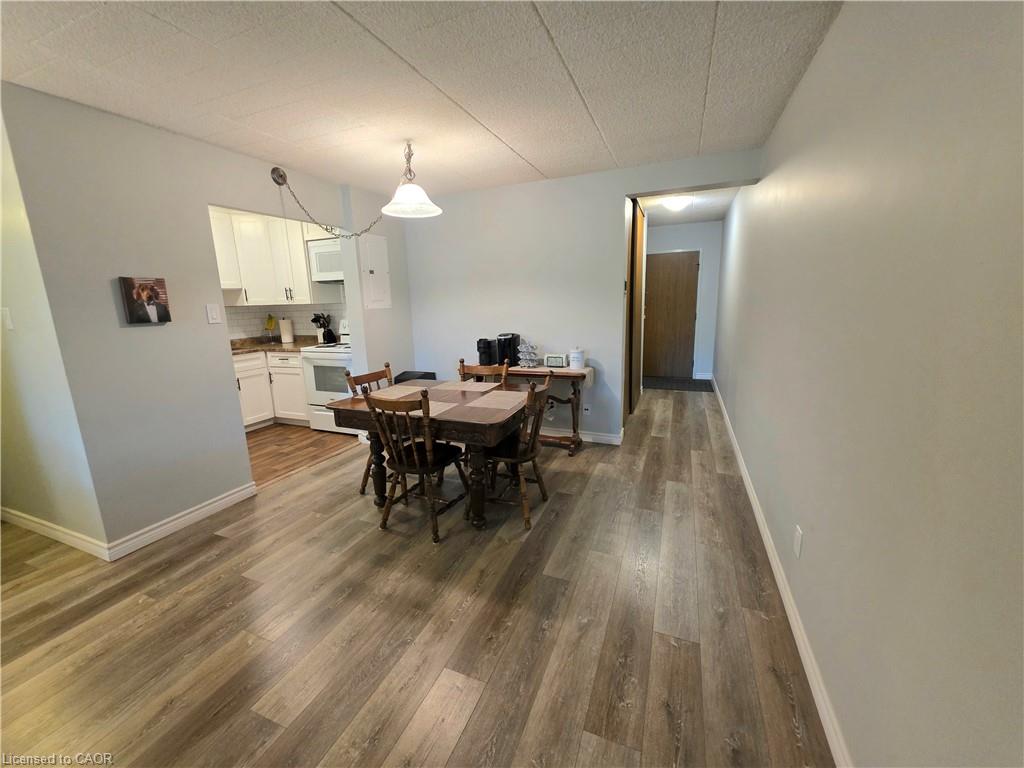 Open-concept living space featuring wood-finish flooring, a dining area with pendant lighting, and a partial view of the kitchen with white cabinetry