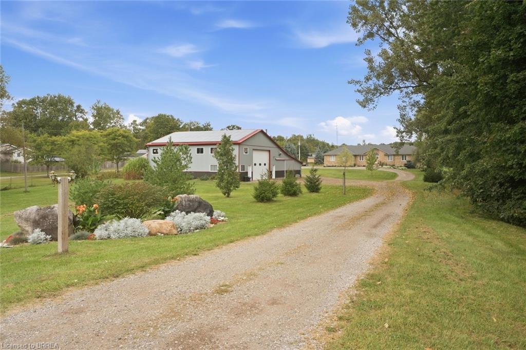 Gravel drive, landscaped rockery, mature trees, detached building with garage door, expansive green lawn