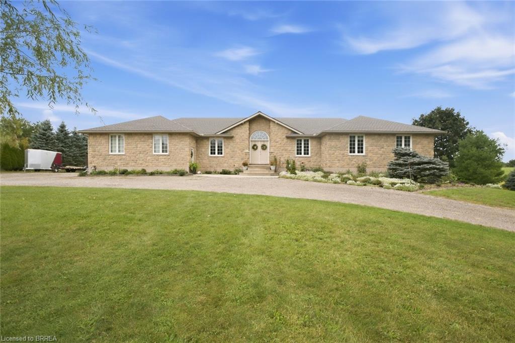 Stone facade residence with a gabled entry, multiple windows, and a gravel driveway