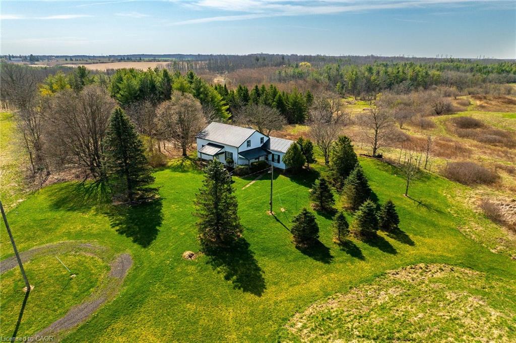 White two-story farmhouse with a dark roof surrounded by extensive green lawn and mature trees