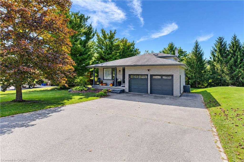 Single-story residence featuring a two-car garage, expansive paved driveway, and mature landscaping