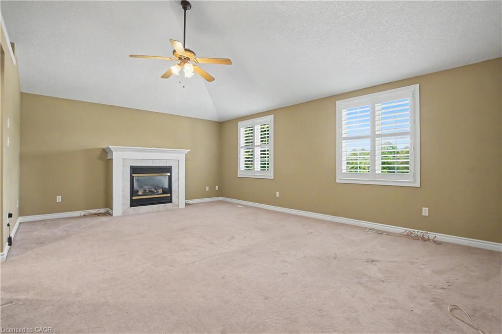 Vaulted ceiling with a ceiling fan, fireplace with a white mantel, and two windows with white plantation shutters