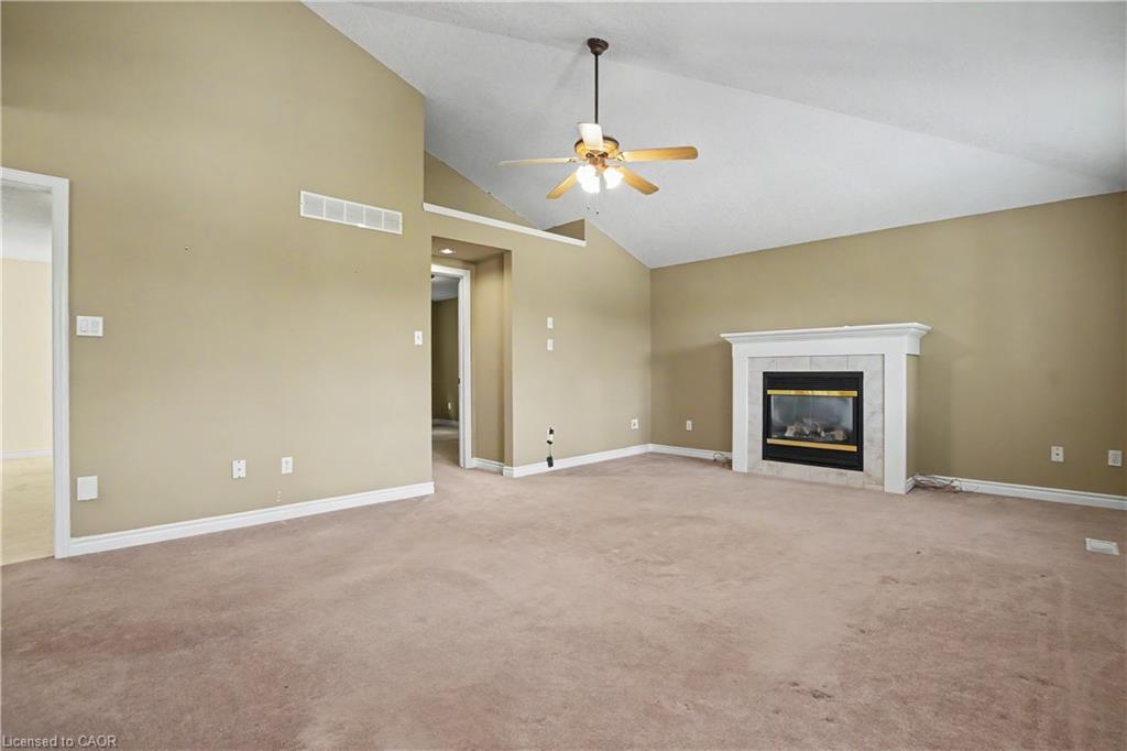 Vaulted ceiling, ceiling fan, carpet flooring, fireplace with white mantel, and light-toned walls