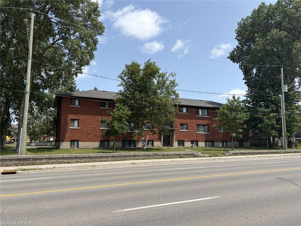 Brick exterior building with multiple windows, featuring mature trees and a paved street frontage