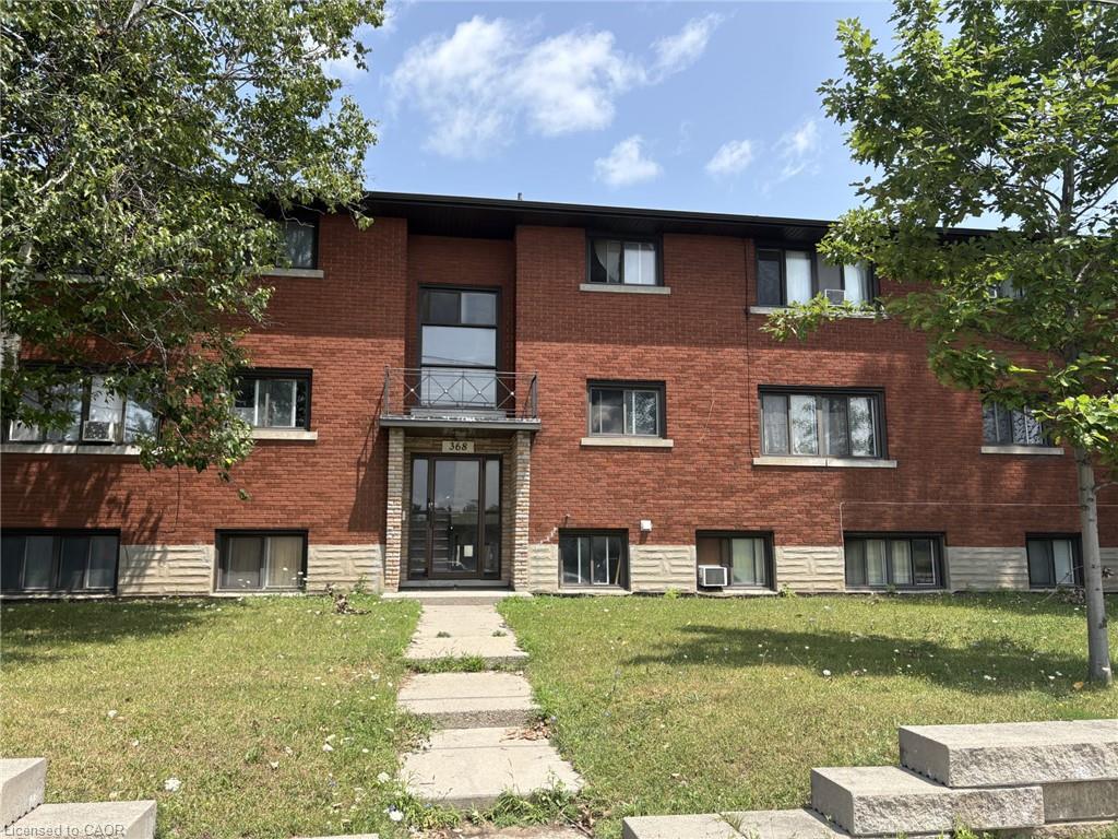 Brick facade building featuring multiple window openings, a central entrance with an overhead canopy, and a decorative wrought iron balcony
