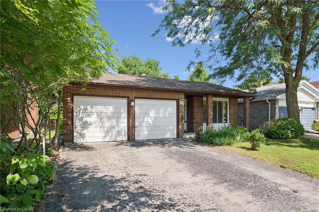 Brick exterior featuring a two-car garage with white doors, a covered porch entry, and mature landscaping