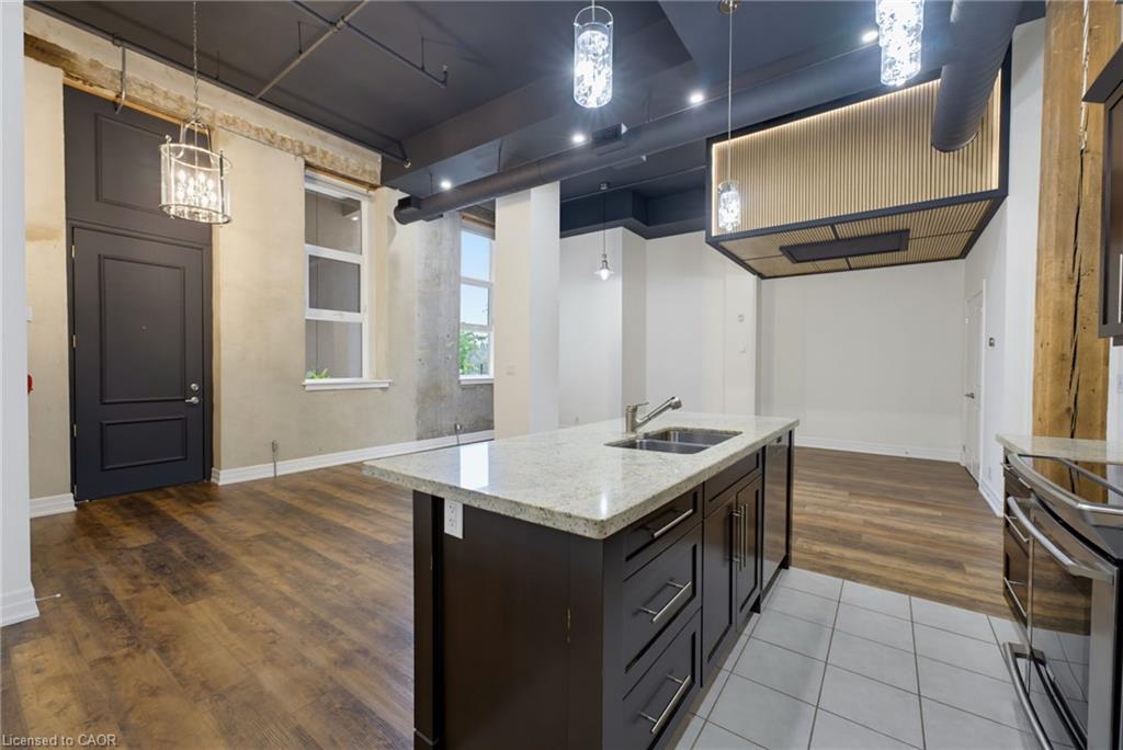 Kitchen island with an undermount double-basin sink and light-toned countertop, dark wood-finish cabinetry, wood-finish flooring, exposed ductwork, and suspended lighting fixtures