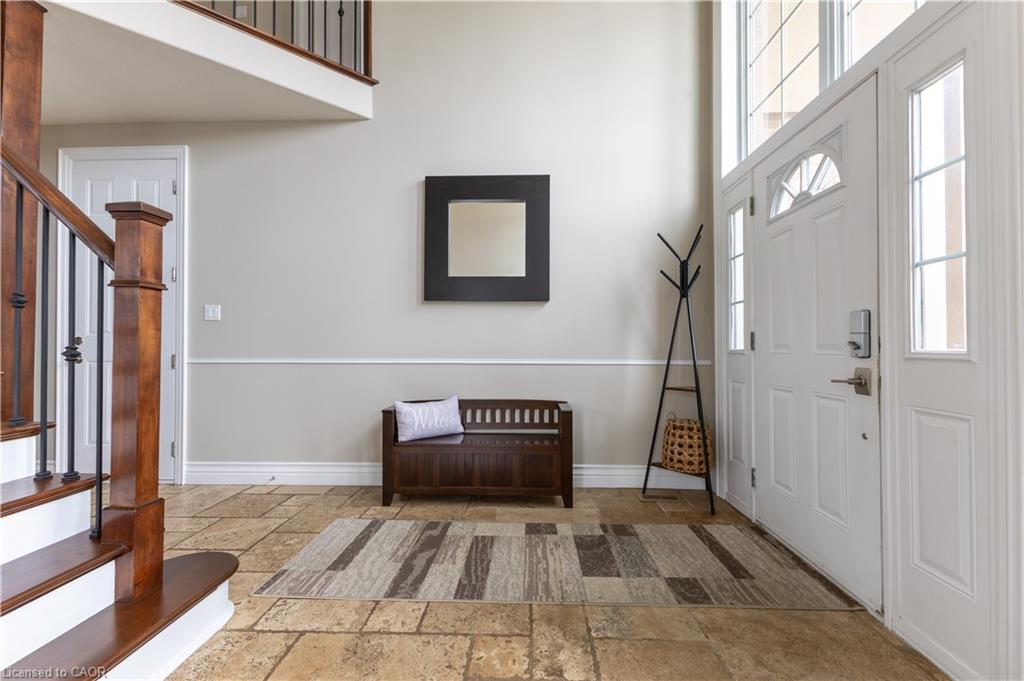 Two-story entryway featuring large format tile flooring, a paneled front door with sidelights, and a wood staircase with wrought iron balusters