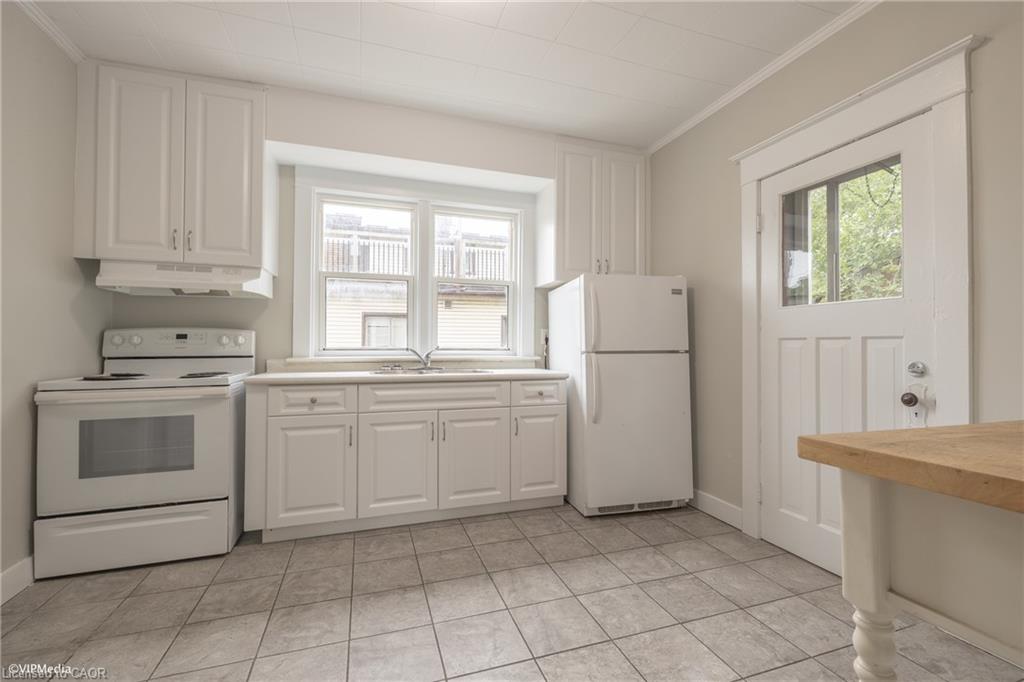 White kitchen cabinetry, tile flooring, window over sink, white appliances, and a paneled entry door with glass insert