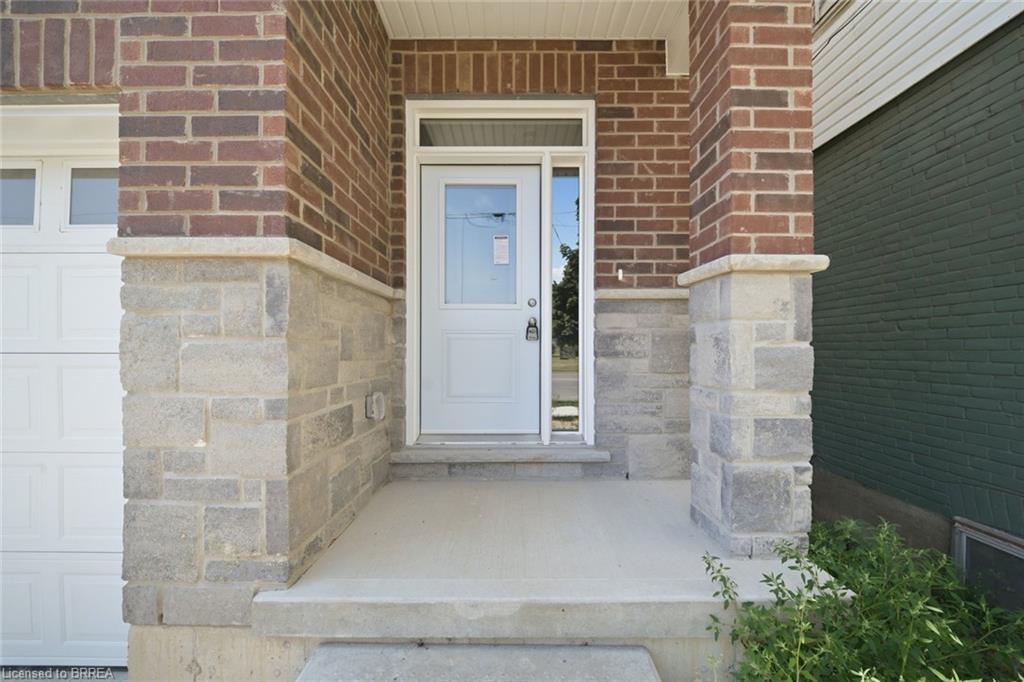 Brick facade with stone accenting, concrete porch, and a white entry door with sidelight
