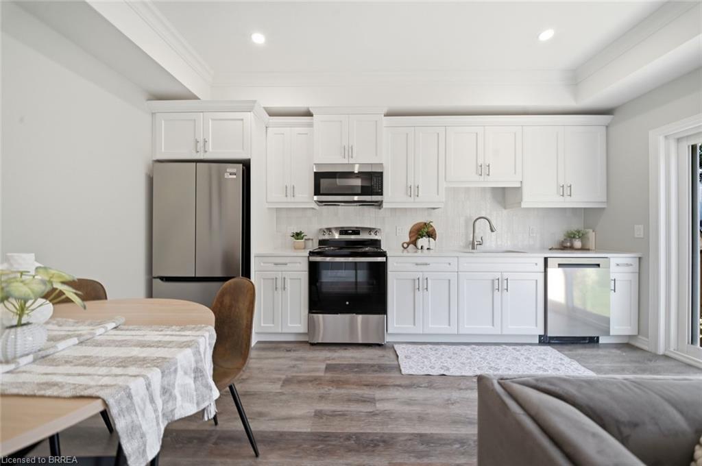 White shaker cabinetry, stainless steel appliances, wood-finish flooring, recessed lighting, and crown molding