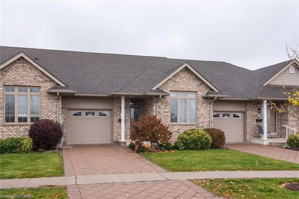 Brick exterior with a shingled roof, featuring a paver driveway, an attached garage, and a covered porch entry