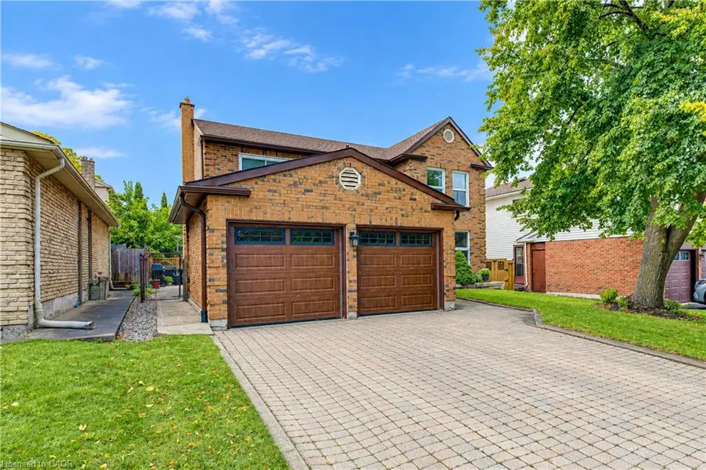 Brick exterior residence featuring a two-car garage with wood-finish doors, a paver driveway, and a manicured lawn