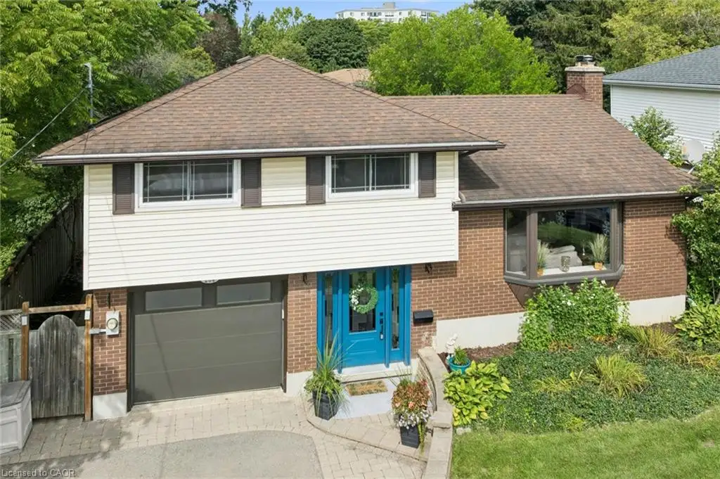 Split-level exterior featuring a combination of brick and horizontal siding, an attached garage, a multi-pane bay window, and a paver driveway