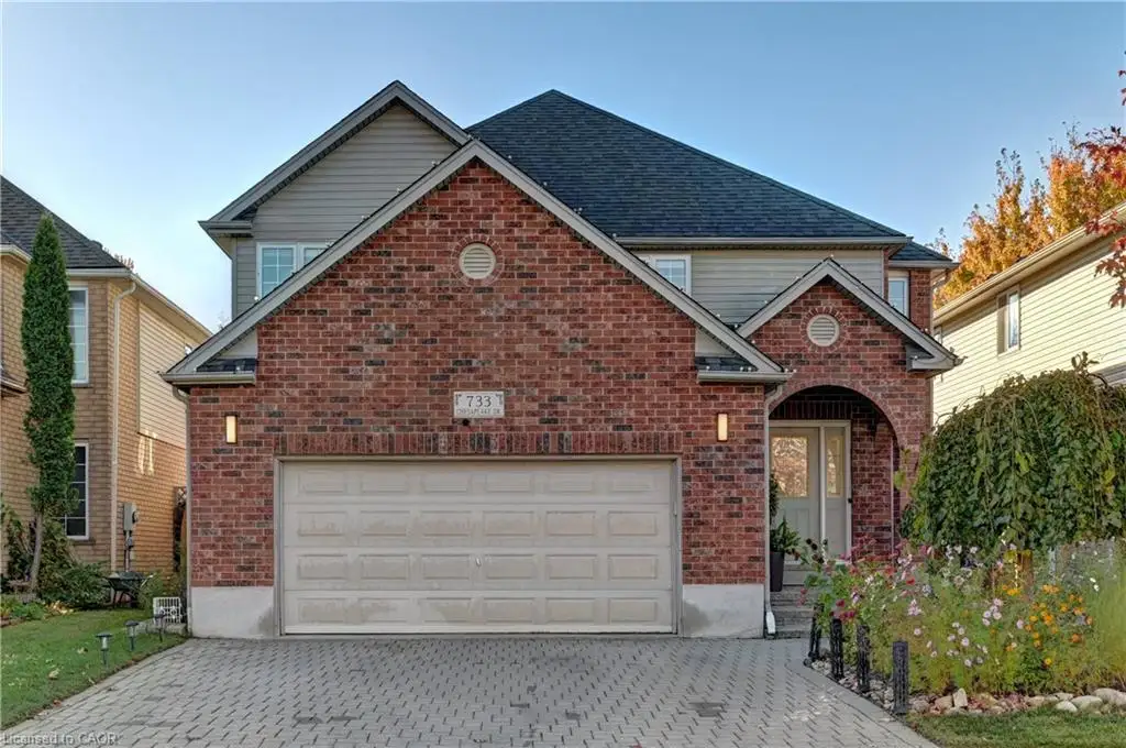 Multi-level exterior featuring a brick facade, vinyl siding, an attached two-car garage, and a paved stone driveway
