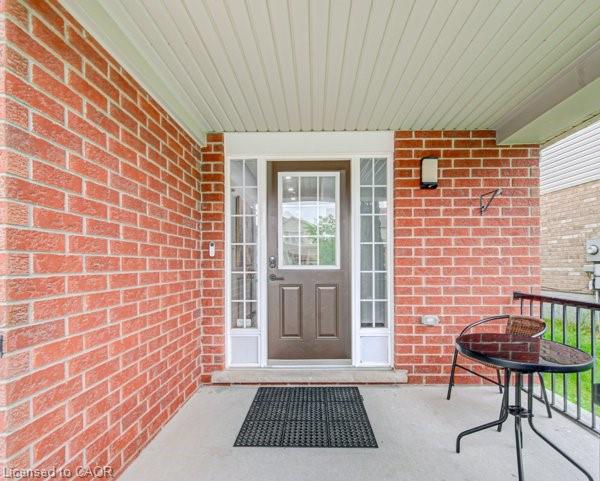 Covered porch entry featuring red brick siding, a brown front door with sidelights, and a concrete landing