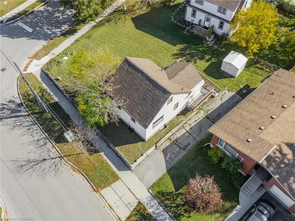 Corner-lot residential property featuring an asphalt driveway, private yard, detached storage structure, and shingled roof