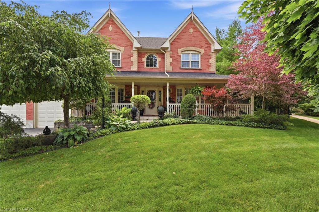 Brick exterior featuring gabled rooflines, a covered front porch with white railings, a two-car garage, and established landscaping