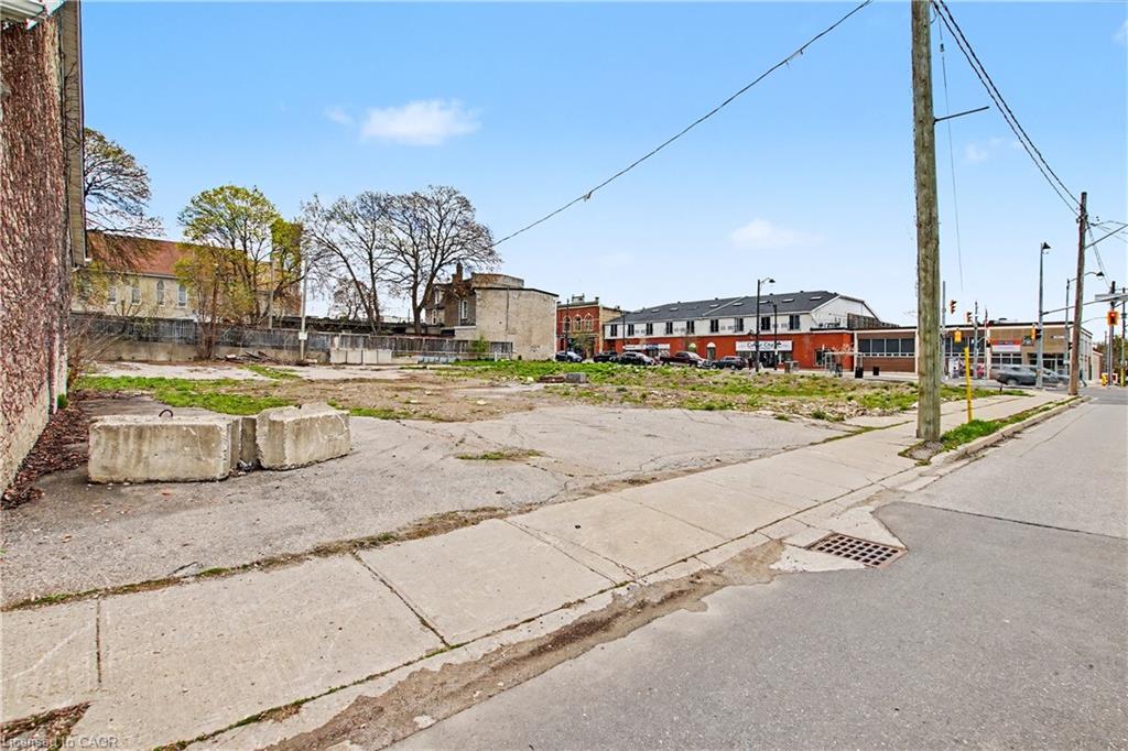 Expansive urban lot featuring a mix of concrete and grass areas, bordered by a brick building and a public sidewalk