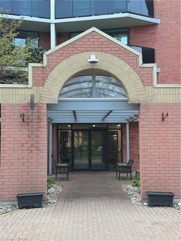 Red brick building entrance featuring a decorative arched brickwork detail, a glass and metal canopy, and large glass double doors