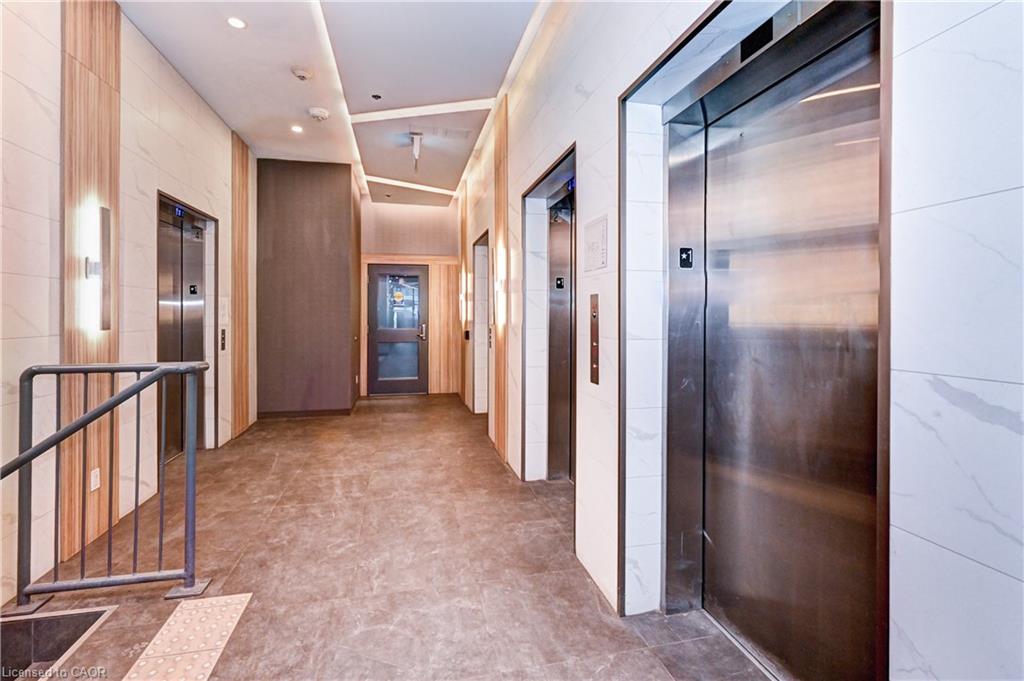 Elevator lobby featuring multiple stainless steel elevator doors, recessed ceiling lighting, wall-mounted sconces, and wood-finish wall panels