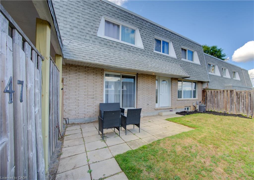 Rear view of property featuring mansard roof, a patio area, roof with shingles, and brick siding