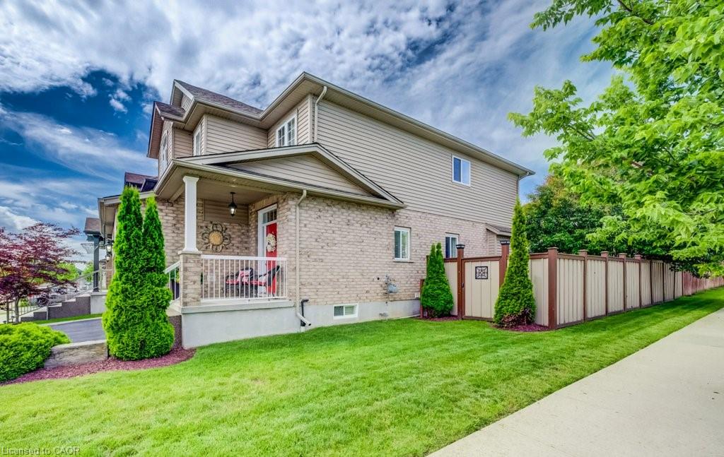 Exterior featuring brick and siding construction, covered front porch with white railing, paved driveway, mature trees, and a privacy fence